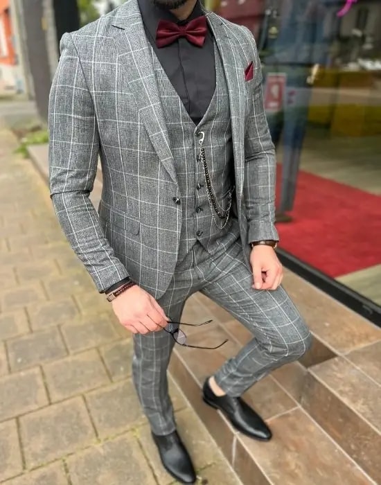 Homme portant un costume gris à carreaux avec nœud papillon.